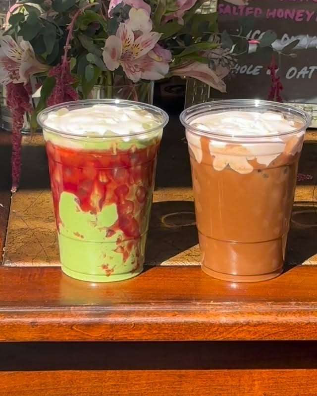 A strawberry matcha and an iced mocha on a wooden counter next to pink lilies